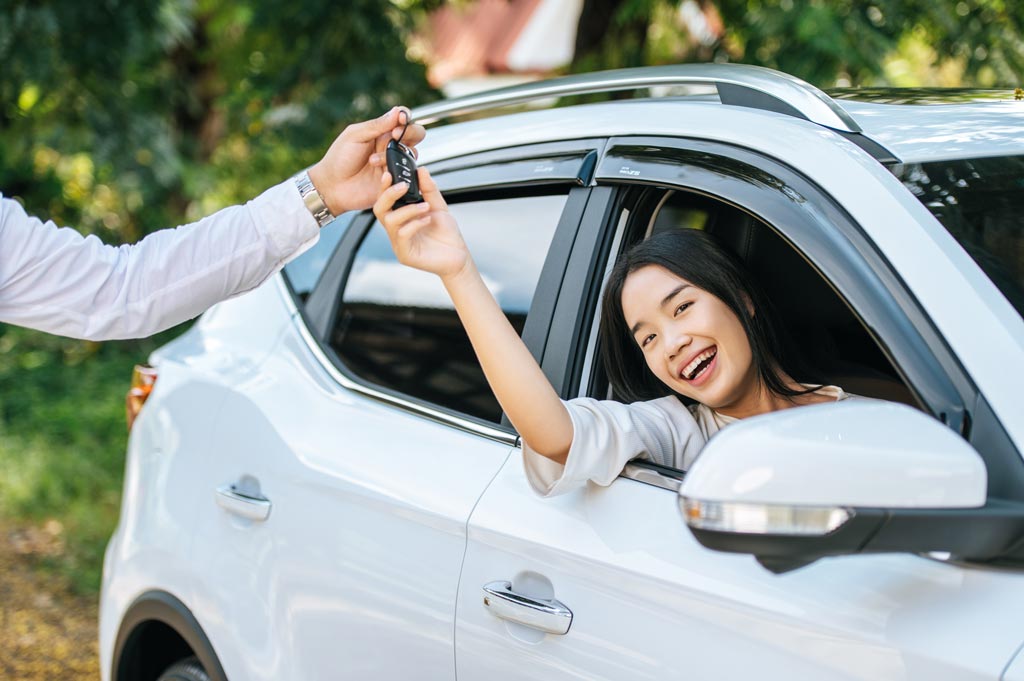 A woman sits in a car and holds out her hand to receive the car keys.